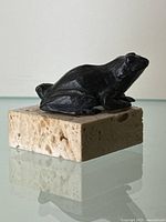 Side view of bronze frog sculpture on travertine base, highlighting details and texture.