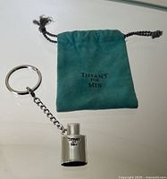 Keychain and original pouch placed flat on a reflective surface showing entire lot