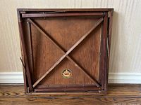 Underside of the folding card table showing wood construction, metal folding mechanism, and Hourd & Company label.