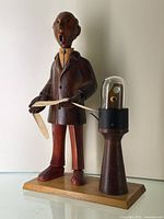 Side angle showing the wooden figurine holding paper tape connected to mechanical device with glass dome.