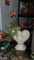 A white ceramic cornucopia planter holding a green pot with aloe vera plants and a decorative butterfly figurine on a wire.