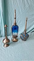 Three antique brass items including two holy water sprinklers and one Moroccan cobalt blue glass perfume bottle with brass holder and stopper.