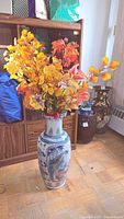 Full view of large porcelain vase filled with colorful faux flowers, showing the flower colors and full vase height.