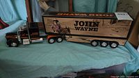 Photo showing full length of black and orange John Wayne themed die-cast model truck and trailer with wood panel design on trailer.