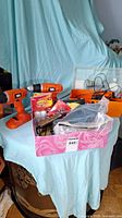 Two Black & Decker cordless drills, assorted chargers, rechargeable batteries, and other items on a table covered by a blue sheet.