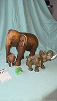 Photo showing all four elephant figurines on blue cloth backdrop, mother and baby wooden elephants, smaller elephant with raised tusks, and small green onyx elephant.