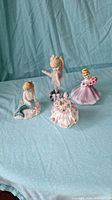 Photo showing four porcelain figures on teal fabric background: mermaid, fairy, ballerina, Dresden style figurines