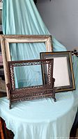 View of all three frames set on a light blue cloth backdrop, showing the carved wooden table frame in front and the other two frames behind