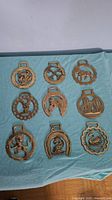 Nine assorted brass horse plaques displayed on a blue cloth, showing each plaque's unique design and size range.