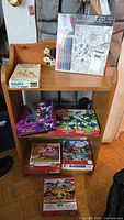 Shelf display photo showing all items: Double Pick-Up Sticks game box, Doodle It canvas art set with markers, and five jigsaw puzzles in boxes of varied themes and sizes.