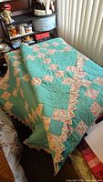 Overall view of the folded quilt draped over furniture showing the teal fabric, floral patchwork pattern, and scalloped border.