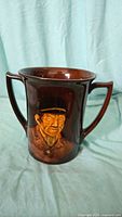 Front view of brown Royal Doulton Kingsware loving cup with Bill Sykes portrait in relief and dual handles.