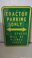 Photo of front side of heavy tin 'Tractor Parking Only' parking sign showing embossed yellow text and arrows on green background.