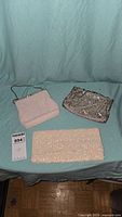 Three vintage beaded evening purses on a light blue cloth background: a white clutch, silver sequin purse, and cream beaded purse with handle.