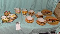 Full lot display showing tea cups, saucers, creamers, sugar bowl, bread plates on light blue cloth background.