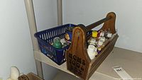 Front view of wooden Mom's tool box filled with various craft paint bottles and blue plastic basket beside it with more containers.