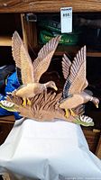 Front view of the wooden sculpture showing two ducks flying above reeds and water lilies