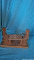 Front view of carved wooden sculpture showing two men seated on stools playing checkers at table.