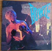 Front cover of David Bowie's 'Let's Dance' album showing Bowie shirtless with boxing gloves and artist name in large turquoise letters.
