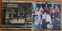 Front covers: Elton John "Tumbleweed Connection" and Billy Joel "Turnstiles" albums placed side by side on wooden surface.