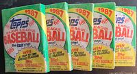 Photo of five unopened 1987 Topps Major League Baseball wax packs, showing front of packs with colorful design and branding details.