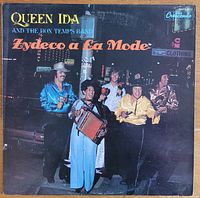 Front cover of the album showing Queen Ida and the Bon Temps Band dressed in colorful clothing with musical instruments outdoors at night.