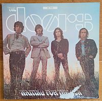 Front cover of The Doors' 1968 album "Waiting for the Sun." Shows band members standing in tall grass with the band logo and album title.