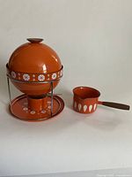 Both fondue kettle on stand with burner and butter warmer saucepan side by side