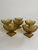 Front view of six amber-colored Czech Art Deco dessert coupes with faceted geometric design and square bases.