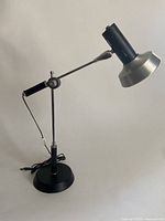 Full view of black and silver articulating desk lamp showing adjustable arm and round base