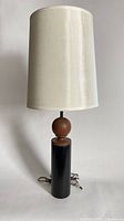 Full view of the lamp displaying its white fabric shade, black cylindrical base, and wooden sphere detail.