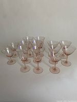 Photo of all 13 pink depression glass stemmed glasses arranged in clusters, showing two distinct styles.