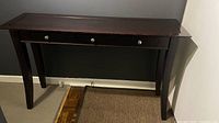 Sofa table showing entire piece with three drawers and dark wood finish, visible wear on top surface.
