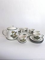 Full coffee set including pot, creamer, cups, saucers, and side plate arranged on table.