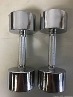 Front view of two shiny chrome dumbbells standing upright showing the knurled handles and solid heads.