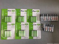 Overview of lot showing all AmazonBasics AAA rechargeable battery packs and loose HDX AA alkaline batteries spread out on a surface