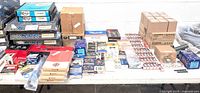 Wide table view showing multiple automotive parts including boxes of spark plugs, brake pads, sensors, filters, and other car maintenance parts.