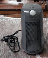 Front view of gray motion sensor heater with control button and cord coiled beside it.