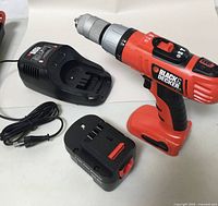 Black & Decker 14.4V cordless drill and separate battery charger and battery on a white surface.