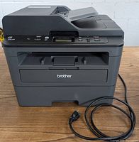Front-facing view of Brother DCP-L2550DW printer showing control panel and paper tray with power cable coiled next to it