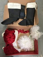 Photo of black boot spats with white fur lining, red Santa hat, curly white beard and hair accessories, and a red fabric piece, presumably trousers or jacket