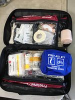 Open emergency first aid kit bag showing various mint condition first aid supplies in clear compartments including bandages, tape, and instant cold pack.