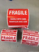 Three rolls of fragile stickers: one 4-inch roll and two 3-inch rolls, red with white text.