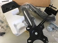 Disassembled dual monitor arm components laid out on a surface with packaging foam and mounting plates visible.
