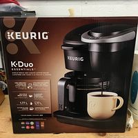 Box front of Keurig K-Duo Essentials coffee maker showing key features: single serve using ground coffee or K-Cup pods, multiple brew sizes (8, 10, 12 cups), 1.77 L capacity, black color.