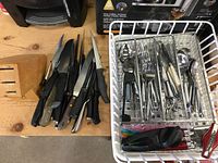 Photo displaying knives in a wooden block holder and a drawer organizer with utensils like spoons, forks, and some kitchen gadgets.