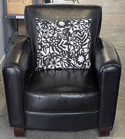 Front view of the black PU leather chair with black and white floral patterned pillow on seat.