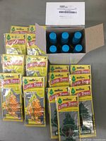 Opened box showing 12 Little Trees Caribbean Colada spray air freshener bottles and packs of orange flame shaped Sliced Little Trees hanging air fresheners