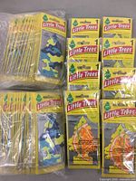 Multiple unopened Little Trees car air fresheners packaged in yellow branded wrappers with tree shape and scent labeling visible.