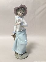 Full front view of the Lladro NAO porcelain figurine showing the girl with a pink bonnet, blue skirt, white top, holding a dove and basket